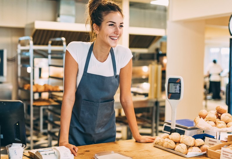 A woman wearing an apron stands on a countertop, surrounded by various baked items in Greater Orlando.